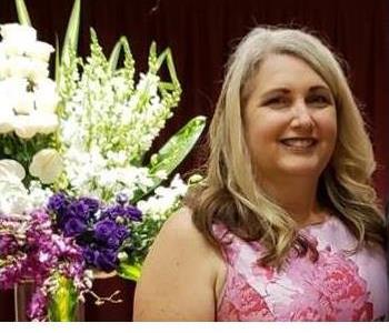 female manager with blonde hair smiling in front of a flowery background